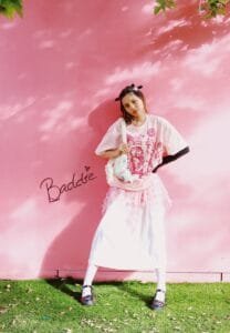 A woman standing in front of a pink wall holding a baseball bat