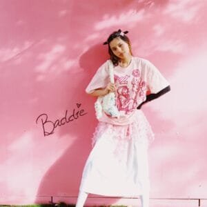 A woman standing in front of a pink wall holding a baseball bat